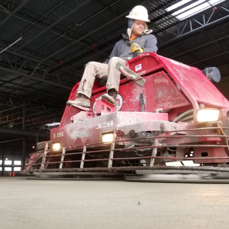 A man on a riding vehicle smoothing concrete